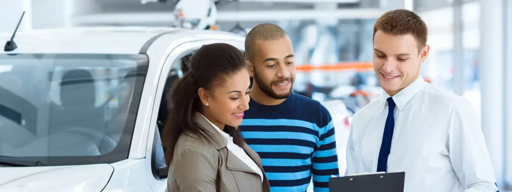 Two people signing a contract with a dealership worker inside a dealership setting, symbolizing the process of buying a car