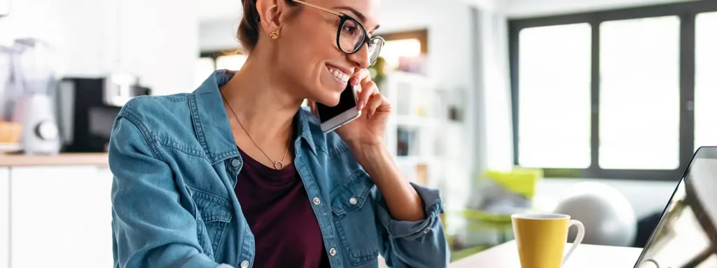 Woman wearing glasses, smiling, and talking on the phone about navigating auto loans while self-employed.